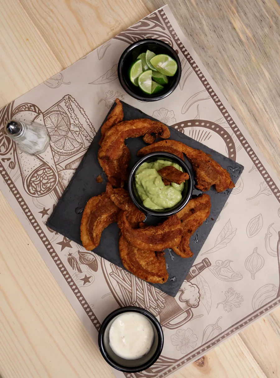 Chicharrón de cerdo sobre pizarra negra con guacamole y limones