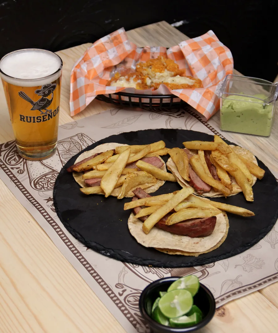 Tacos sobre plato negro con papas fritas, guacamole y limón