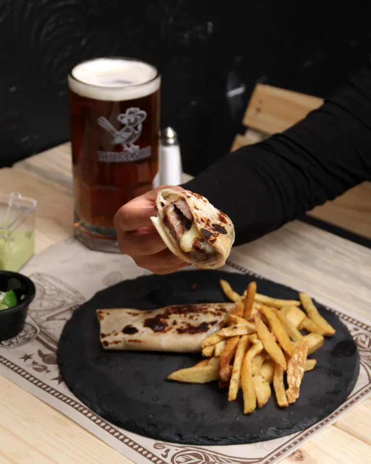 Burrito norteño con queso y papas, junto a una cerveza obscura